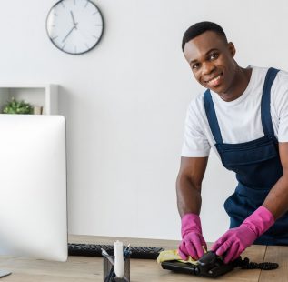 Selective focus of smiling african american cleaner cleaning telephone with rag on office table